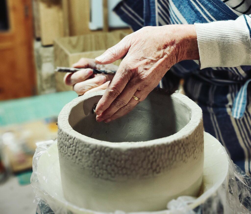 Mains d'une personnes lors d'un atelier, façonnant un pot fait au colombin, destiné à être suspendu.